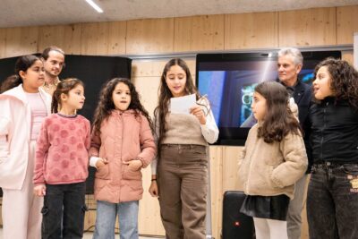 Une fille entourée d'autres enfants récite quelques mots sur la laïcité sous le regard de Daniel Iché et du vidéaste - Agrandir l'image 2 sur 5, fenêtre modale